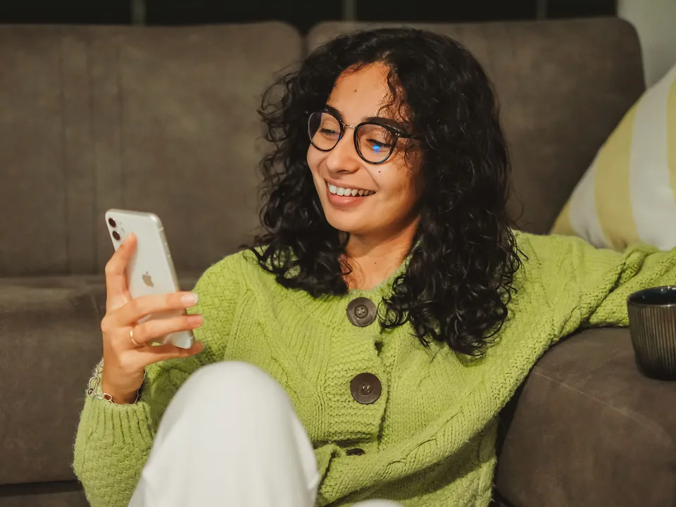 Imagen referencial: mujer sonriendo mientras mira su celular en el sofá